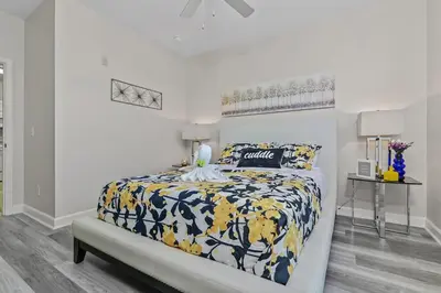 a white bedroom with a bed with a blue and yellow comforter at Stylish 3BR Condo Near Disney Pool, Gym & More! in Kissimmee