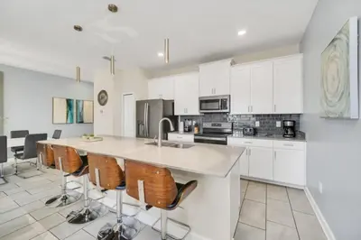 a kitchen with white cabinets and a island with bar stools at Retreat & Relax Screened In Pool Home Kid Rooms townhouse in Kissimmee