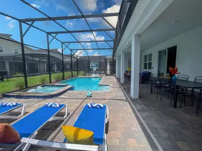 a patio with a pool with blue chairs and a basketball hoop at Gorgeous 6BR at Storey Lake next to Disney - 2850 in Kissimmee