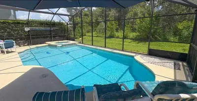 a large swimming pool with chairs and an umbrella at 648 - Spacious 6-Bedroom Emerald Island Retreat with Pool, Spa & Games Room Near Disney in Kissimmee