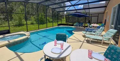 a swimming pool with chairs and a table and an umbrella at 648 - Spacious 6-Bedroom Emerald Island Retreat with Pool, Spa & Games Room Near Disney in Kissimmee