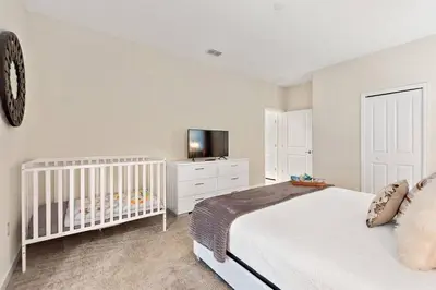 a white bedroom with a crib and a tv at Bookmark Villa 8Q no Storey Lake c/ Piscina in Kissimmee