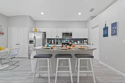 a kitchen with white cabinets and a large island with bar stools at Finest renovated w Pool, Game rm, 4 Mi to Disney in Kissimmee