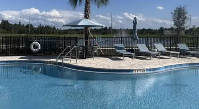 a pool with chairs and an umbrella and a table with an umbrella at Landing Beautiful 2BD in Kissimmee in Kissimmee