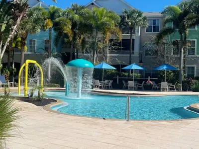 a pool with a fountain and tables and blue umbrellas at Magical Apartment DisneyFree ShuttleFree parking in Kissimmee