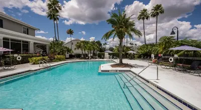 a large swimming pool with palm trees and a building at Quiet Gated Condo Near Universal with Pool and View in Orlando