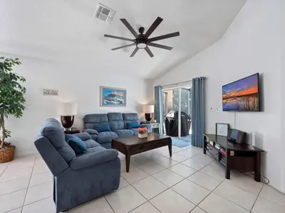 a living room with a blue couch and a ceiling fan at Oasis Key Retreat by PropertyChekker! in Kissimmee