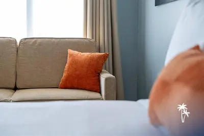 a couch with an orange pillow sitting next to a window at Superior Central Condo with Balcony 7 Min to Universal in Orlando