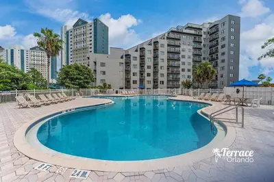 a swimming pool with chairs and buildings in the background at Superior Central Condo with Balcony 7 Min to Universal in Orlando