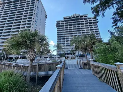 a wooden walkway with two tall buildings and palm trees at Blue Heron Beach Resort 1-809 in Orlando