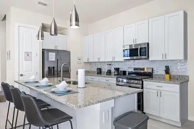 a kitchen with white cabinets and a large island with chairs at 5 Suites Sleeps 14 Lion King Mickey Theme in Orlando