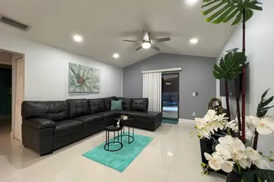 a living room with a black leather couch and a ceiling fan at Beautiful pool home 15 minutes from Disney! in Kissimmee
