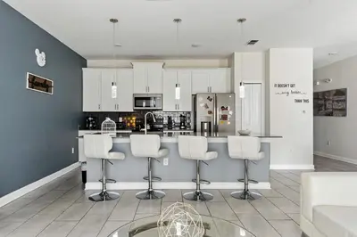 a kitchen with white cabinets and a bar with stools at Townhome 4Q c/ Piscina Privativa no Storey Lake in Kissimmee