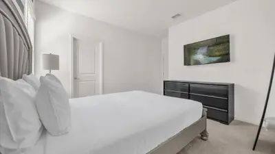 a white bedroom with a bed and a painting on the wall at Upstay Spacious Villa w Pool, Hot Tub & Game Room in Kissimmee
