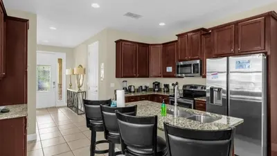 a kitchen with wooden cabinets and a bar with chairs at Vila 7Q Temática c/ Piscina – 6mi Disney in Orlando