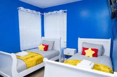 two beds in a blue room with red and yellow pillows at 3BR Disney Home with Pool , Arcade and Hot Tub in Kissimmee