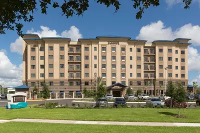 a large tan building with cars parked in a parking lot at Staybridge Suites Orlando at SeaWorld by IHG - Free Breakfast & Shuttle to SeaWorld Parks in Orlando