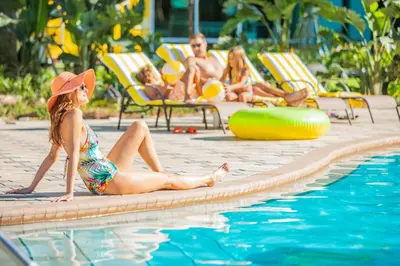 a woman in a hat sitting next to a swimming pool at Hotel Landy Orlando Universal Blvd, a Tribute Portfolio Hotel in Orlando