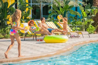 a group of people sitting in lawn chairs by a swimming pool at Hotel Landy Orlando Universal Blvd, a Tribute Portfolio Hotel in Orlando