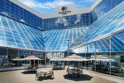 a large glass building with tables and umbrellas at DoubleTree by Hilton Orlando Airport Hotel in Orlando