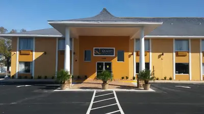 a yellow hotel with palm trees in a parking lot at Quality Inn & Suites Heritage Park in Kissimmee