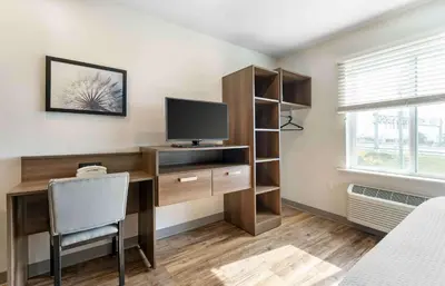 a room with a computer desk with a tv and a window at Extended Stay America Select Suites - Orlando - Airport in Orlando