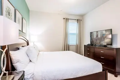 a bedroom with a white bed and a tv on a dresser at Vibrant Elite Home With Theater Room And Waterpark & Resort Access Near Disney At Encore Resort - 7603Mc in Orlando