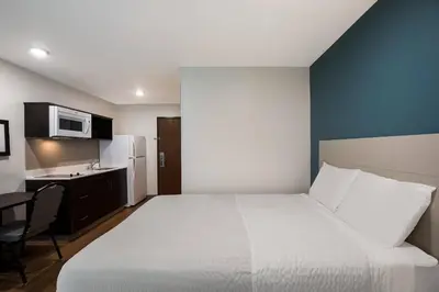 a bedroom with a white bed and a kitchen at WoodSpring Suites Orlando West - Clermont in Clermont