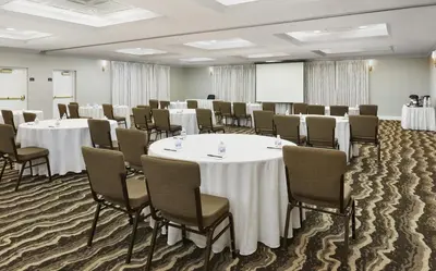 a conference room with tables and chairs and a screen at Staybridge Suites Orlando South by IHG in Orlando
