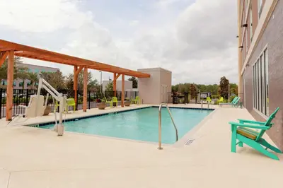 a swimming pool with a green chair next to a building at Home2 Suites By Hilton Orlando South Park - Near Epic Universe in Orlando