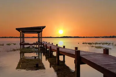 a dock on a lake with the sunset in the background at Spacious Lakefront House with Pool, Hottub, & Boating in Orlando
