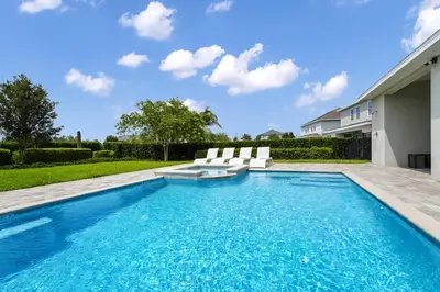 a swimming pool with two white chairs and a house at Striking Home With Games, Outdoor Kitchen Near Disney With Waterpark & Resort Access At Encore Resort - 7742Ff in Kissimmee