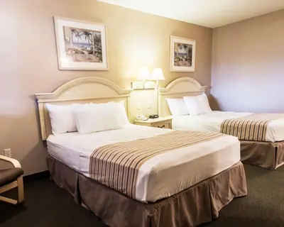 a hotel room with two beds and a chair at Rodeway Inn Apopka South in Orlando