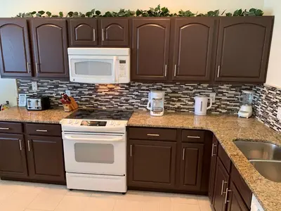 a kitchen with brown cabinets and a white stove and microwave at Windsor Hills Resort 5BR Villa, Amenities, Private Pool & Water Park, Near Disney, Sea World, Universal in Orlando