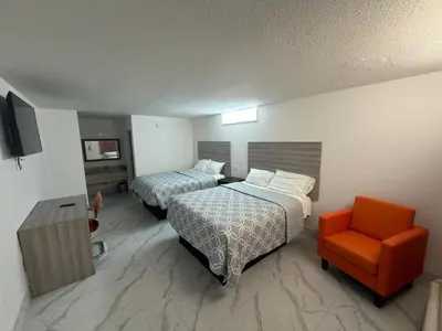 a hotel room with two beds and an orange chair at Apollo Inn - Downtown in Kissimmee