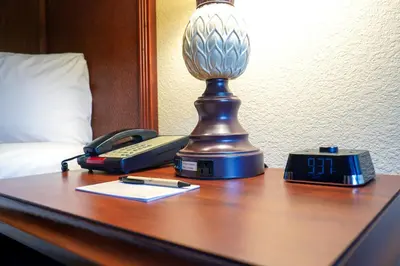 a desk with a lamp and a phone on a bed at Rosen Inn Closest to Universal in Orlando