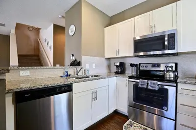 a kitchen with white cabinets and stainless steel appliances at Amazing townhouse fits 10 in gated community 10 min to Disney! in Kissimmee