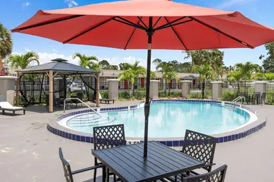a table with a red umbrella next to a swimming pool at Super 8 by Wyndham Kissimmee-Orlando in Kissimmee