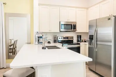 a kitchen with white cabinets and a stainless steel refrigerator at Playa Verde Cottage With Private Hot Tub Near Disney With Margaritaville Resort & Island H2O Access - 8028Dr in Orlando