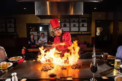 a chef cooking over a fire in a kitchen at Mai Hana Hotel and Suites I Drive-Theme Parks in Orlando