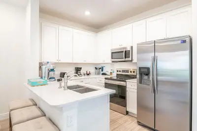 a kitchen with white cabinets and a stainless steel refrigerator at Sunset Sands Cottage Near Disney With Margaritaville Resort & Island H2O Access - 8065Dr in Orlando