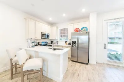 a kitchen with white cabinets and a stainless steel refrigerator at Flip Inn Paradise Cottage With Private Hot Tub Near Disney With Margaritaville Resort & Island H2O Access - 8004Sb in Orlando