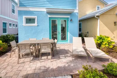 a patio with a table and chairs in front of a blue house at Ocean Blue Cottage Near Disney With Margaritaville Resort & Island H20 Waterpark Access - 2971La in Orlando