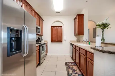 a kitchen with wooden cabinets and a stainless steel refrigerator at Cozy Condo wPrivate Balcony & FREE Resort Access in Orlando