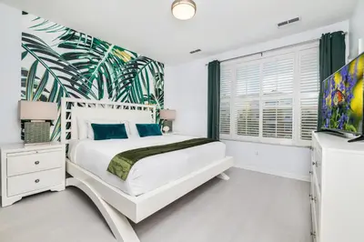 a bedroom with a white bed with a tropical wallpaper at Updated Vista Cay Townhome, 10 min from Universal in Orlando