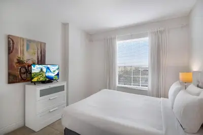 a white bedroom with a bed and a television at Updated Condo Near Conv Ctr, I-Drive & Universal in Orlando