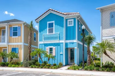 a blue house with palm trees in front of condos at Blue Shores Cottage Near Disney With Margaritaville Resort & Island H2O Access - 8079Kd in Orlando