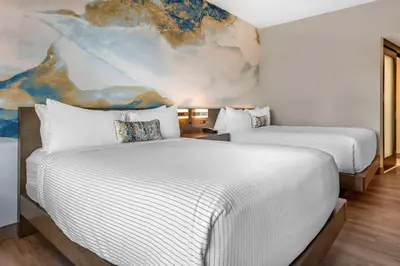 two beds in a hotel room with a painting on the wall at Cambria Hotel Orlando Airport in Orlando