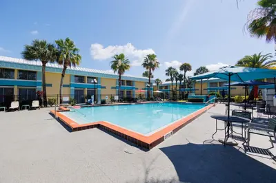 a large swimming pool with tables and umbrellas next to a building at Garnet Inn & Suites, Orlando in Orlando