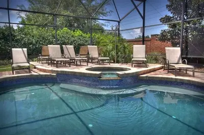 a swimming pool with chairs and a table at Mickeys Getaway - CUSTOM 8BR Luxurious Retreat Pool Hot Tub Theater RM Gym! Outdoor Kitchen 2 Miles to Disney in Orlando